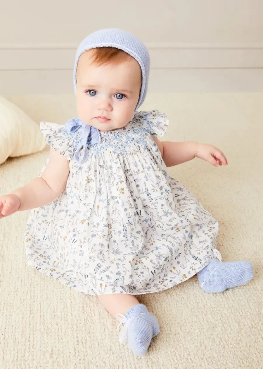Pepa London Ellis Sleeveless Dress with Bloomer and Bows in Blue Made with Liberty Fabric (1-12m) | Openwork Detail Baby Cardigan in Blue (1-12mths) | Lace Detail Knitted Bonnet in Blue (1-6mths) | Lace Detail Knitted Booties in Blue | Ellis Dummy Clip in Blue Made with Liberty Fabric | BIBS Dummy in Blue