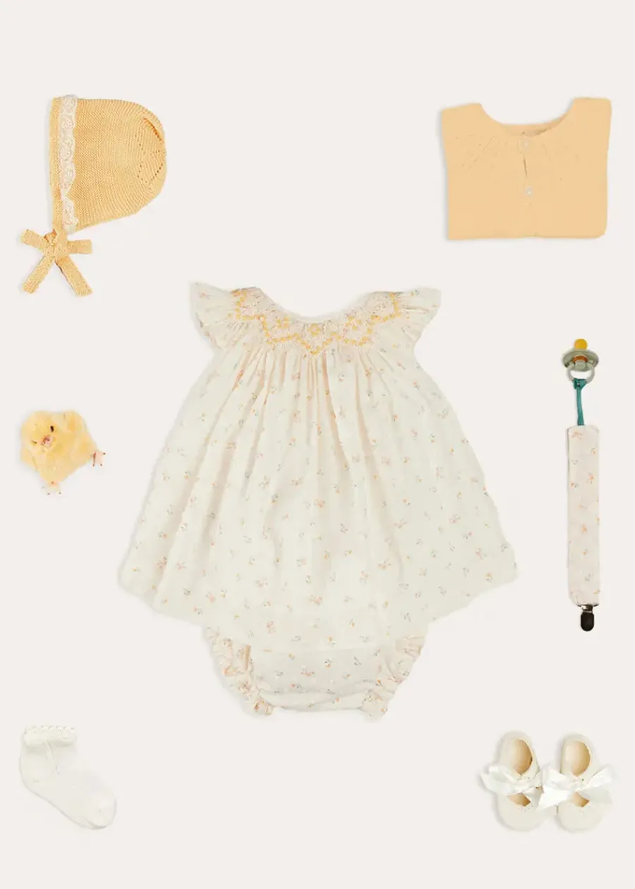 Pepa London Esme Floral Hand Smocked Sleeveless Dress With Bloomers in White (1-12mths) | Openwork Detail Cotton Baby Cardigan in Tangerine (1-12mths) | Lace Detail Knitted Bonnet in Tangerine (1-12mths) | Celebration Ribbon Detail Mary Jane Pram Shoes in Beige (17-20EU) | Esme Floral Dummy Clip in White | Openwork short socks White (0mths-8yrs) | Chick Toy in Yellow | BIBS Dummy in Sage Green
